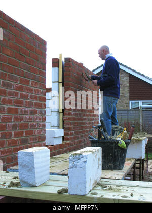 Builder / lavoratore edile la costruzione di un muro di mattoni mattoni di cementazione in su una estensione o la nuova proprietà modello di rilascio Foto Stock