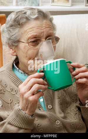 Donna anziana usando un inalatore di vapore inalazione di un decongestionante per raffreddori e bronchiti modello di rilascio Foto Stock