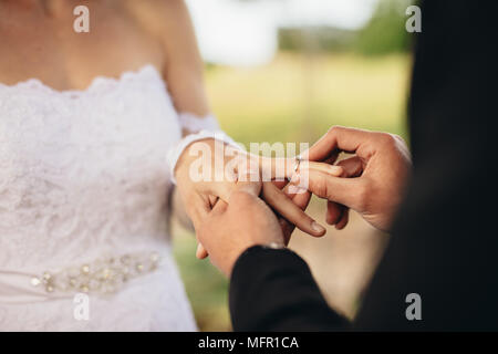 Primo piano della giovane scambiare gli anelli di nozze durante la loro cerimonia di nozze all'esterno. Ritagliato shot di groom mettendo un anello di nozze al dito del b Foto Stock