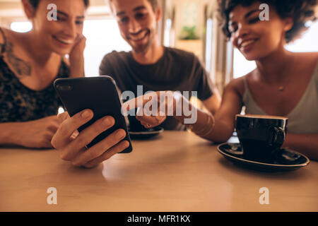 Gruppo di amici riuniti presso la caffetteria e guardando il telefono cellulare. Uomo che mostra il suo telefono con gli amici con una donna rivolta a schermo mobile. Foto Stock