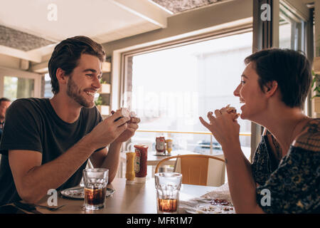 Coppia felice di mangiare hamburger e godendo al cafe'. Giovane uomo che parla con la sua fidanzata e sorridere mentre per mangiare in un ristorante. Foto Stock