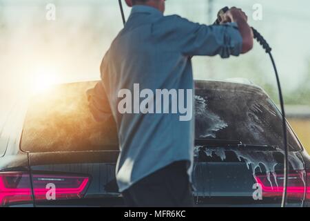 Uomini caucasici il lavaggio della sua auto utilizzando acqua ad alta pressione della rondella. Lavaggio auto tema. Foto Stock