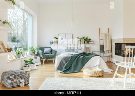 Il bianco e il legno interno camera da letto con un grande letto matrimoniale, caminetto, finestra, rug, poltrona e scaletta Foto Stock