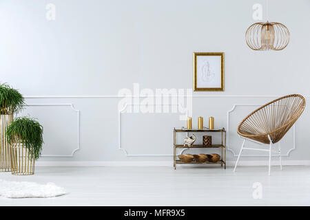 Moderna sedia in vimini e disegno in cornice dorata su un bianco, parete vuota in un elegante salotto interno Foto Stock