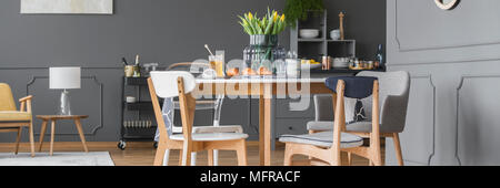 Lampada su uno sgabello nella spaziosa sala da pranzo interno con tavolo in legno con tulipani gialli accanto a un cabinet grigio Foto Stock