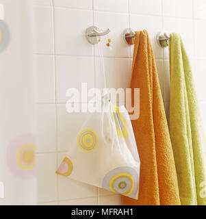 Accessori per il bagno e asciugamani appesi a ganci di acciaio su bianco parete piastrellata Foto Stock
