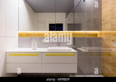 Il bianco e il grigio bagno interno con accenti di colore giallo sul armadi, acciaio rubinetto e lavabo in ceramica Foto Stock