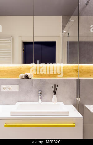 Porta la riflessione nello specchio sopra lavabo bianco con acciaio inossidabile rubinetto in bagno luminoso interno Foto Stock