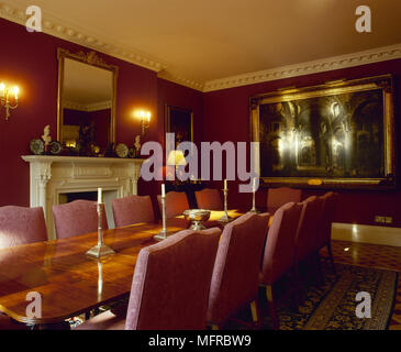 Red sala da pranzo con tavolo da pranzo in legno, sedie imbottite, camino, illustrazioni e accesa candelabri a muro. Foto Stock