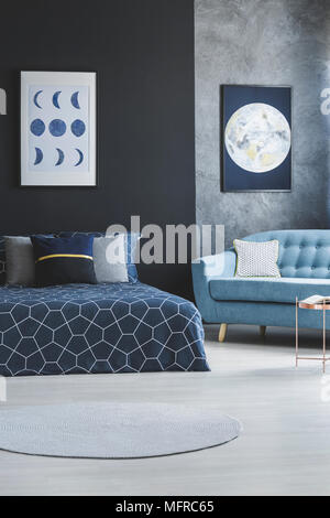 Divano blu accanto al letto modellato in spazio aperto interno con luna poster sul muro grigio Foto Stock