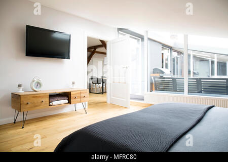 Vista laterale di interiore camera da letto con TV, armadio in legno e grandi finestre in appartamento Foto Stock