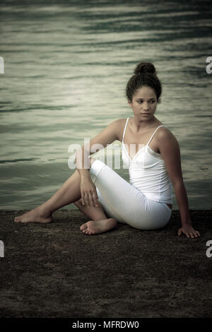 Una giovane donna è seduta al lago Foto Stock