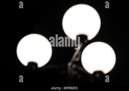 Basso-chiave fotografia di una luminosa sfocata lampione con tre lampade su uno sfondo nero in primo piano Foto Stock