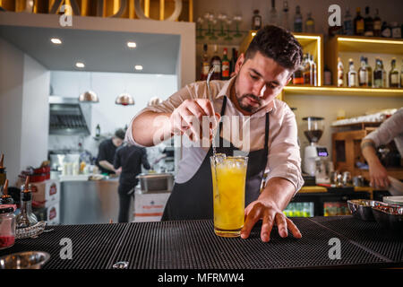 Il barista dietro il bancone di agitazione una bevanda analcolica con acciaio cucchiaio swizzle Foto Stock