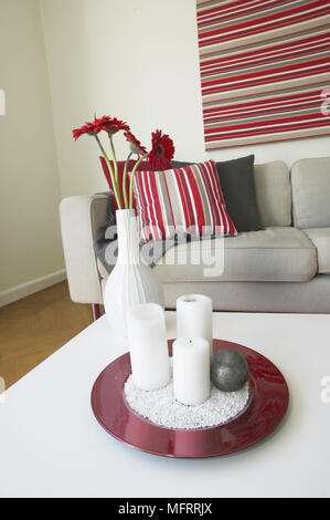 White tavolino con piastra di candele e vaso di fiori nella parte anteriore del divano rosso con cuscini a righe Foto Stock