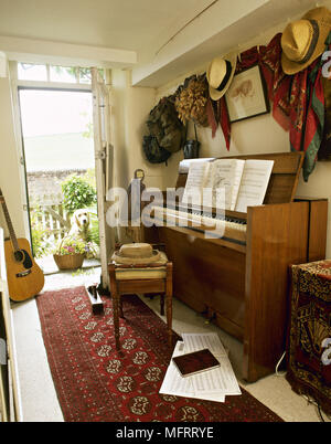 Paese corridoio con pianoforte verticale sgabello spartiti appendere cappelli e un cane guardando attraverso la porta aperta. Foto Stock