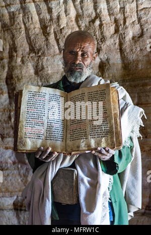 Un sacerdote ortodosso della Chiesa rock Mikael Mellehayzengi mostra un libro scritto a mano su carta pergamena nella chiesa lingua Ge'ez Foto Stock