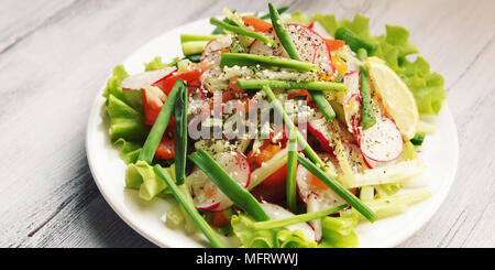 La molla insalata di verdure sulla piastra bianca. Il ravanello, pomodori, sedano e il cetriolo. E rabboccato con semi di sesamo. Piatto vegetariano sul bianco tavolo in legno. C Foto Stock
