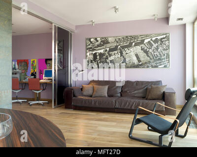 Zona salotto grande foto sopra il lettino su pavimento di legno accanto alla home office space con illustrazioni a colori Foto Stock