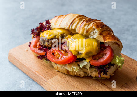 Croissant Burger con polpette di carne, formaggio Cheddar e pomodori. Fast Food. Foto Stock