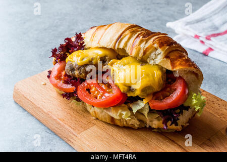 Croissant Burger con polpette di carne, formaggio Cheddar e pomodori. Fast Food. Foto Stock