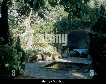 Un giardino con una appartata patio pavimentato area, fontana e laghetto, pentole, arbusti, Foto Stock