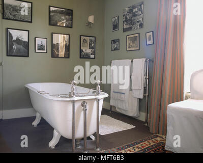 Un tradizionale bagno di colore verde con freestanding roll top vasca da bagno, pattern tende, una raccolta di fotografie sulla parete Foto Stock