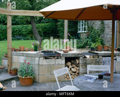 Cortile interno con un mattone barbecue esterno, patio in lastricato e un tavolo e sedie sotto un ombrello. Foto Stock