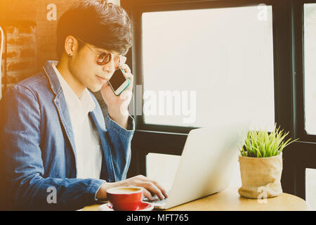 Urban business man lavorando sul computer portatile in viaggio all'interno di in un coffee shop all'aeroporto. Asian Casual giovane imprenditore tuta da indossare giacca e occhiali da sole.Ha Foto Stock