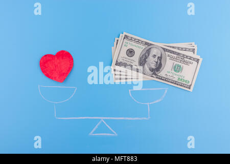 Il denaro e il cuore sulla bilancia su sfondo blu Foto Stock