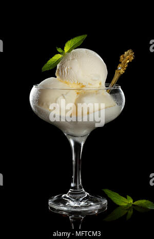 Gelato guarnite con foglioline di menta in un bicchiere a calice, acquisiti su uno sfondo nero Foto Stock