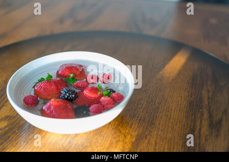 Fragole, lamponi e more flottante in una tazza di acqua Foto Stock