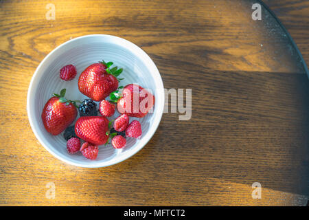 Fragole, lamponi e more flottante in una tazza di acqua Foto Stock