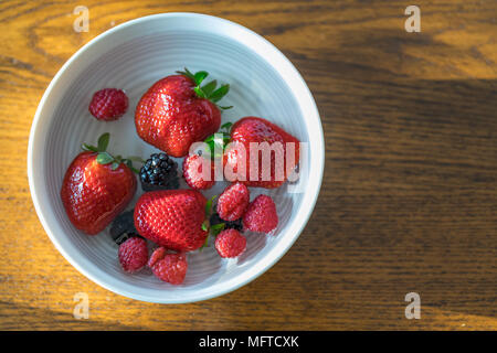 Fragole, lamponi e more flottante in una tazza di acqua Foto Stock