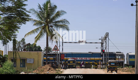 Il Karnataka, India - 2 Marzo 2018: treni passeggeri passando al di sopra di un passaggio a livello in zona rurale Foto Stock