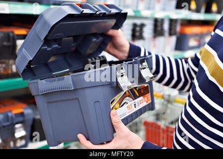 L'uomo acquirente sceglie una cassetta degli attrezzi di plastica in negozio Foto Stock