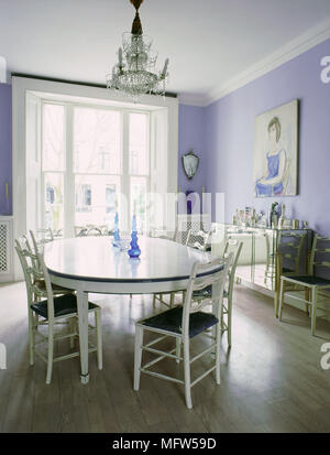 Tradizionale sala da pranzo ovale con tavolo da pranzo e sedie laterali a specchio armadio lampadario di cristallo pavimento in legno e una soleggiata baia finestra. Foto Stock