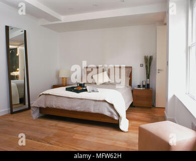 Dettagli di una moderna camera da letto con un grande specchio di lunghezza completa accanto a un letto doppio con due laterali in legno tavoli e una piazza sedile in primo piano. Foto Stock