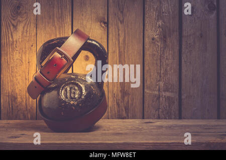 Vecchio kettlebell con cintura di pelle su uno sfondo di legno, padre giorno concept Foto Stock