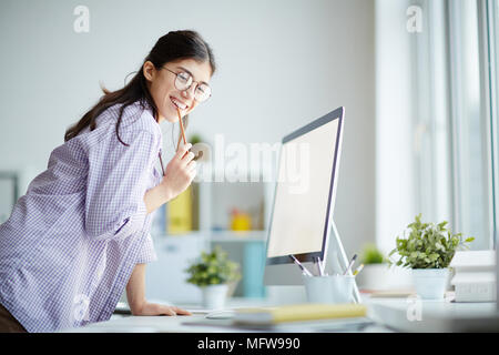 Ritratto di successo della giovane designer in piedi nella parte anteriore del computer e sorridente Foto Stock