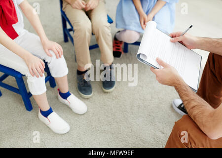 Maschio Unreсognizable docente in possesso di appunti con il piano della lezione e comunicante con i ragazzi in classe Foto Stock