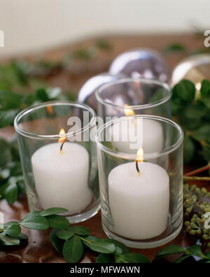 Candele accese in vetro portacandele con Natale baubles dietro Foto Stock