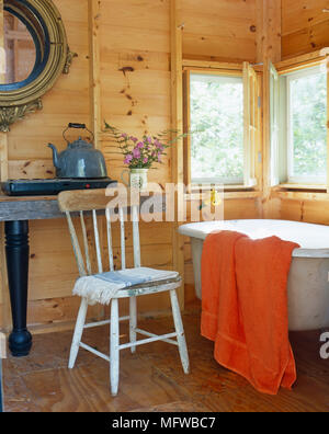 Rustico sedia di legno accanto al vecchio stile roll top vasca da bagno Foto Stock