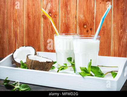 Noce di cocco latte vegano coctail in vetro su sfondo di legno. Foto Stock