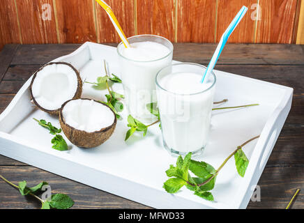 Noce di cocco latte vegano coctail in vetro su sfondo di legno. Foto Stock