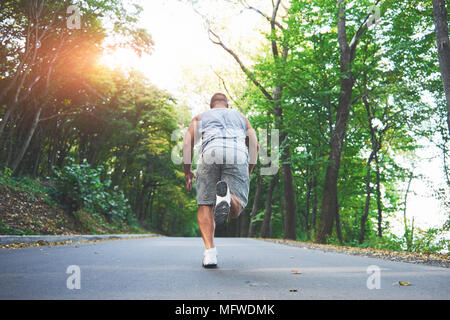 Outdoor cross-country in esecuzione nella nozione di esercizio, fitness e uno stile di vita sano. Close up dei piedi di giovani runner uomo che corre lungo la strada nel parco Foto Stock