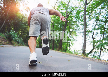 Outdoor cross-country in esecuzione nella nozione di esercizio, fitness e uno stile di vita sano. Close up dei piedi di giovani runner uomo che corre lungo la strada nel parco Foto Stock