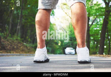 Outdoor cross-country in esecuzione nella nozione di esercizio, fitness e uno stile di vita sano. Close up dei piedi di giovani runner uomo che corre lungo la strada nel parco Foto Stock