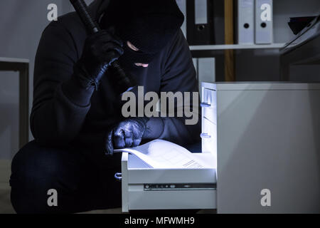 Ladro tenendo la torcia elettrica rubare Documento dal cassetto in ufficio Foto Stock