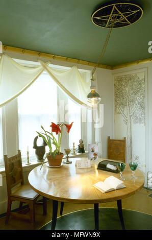 Sala da pranzo moderna verde con il soffitto dipinto, tende bianche su una finestra piena di sole e di un tondo in legno tavolo da pranzo e sedie. Foto Stock